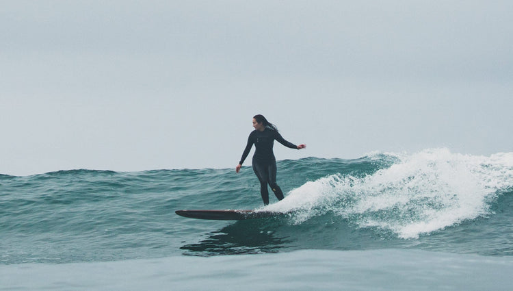 A female surfer wearing a backzip wetsuit while surfing on a longboard