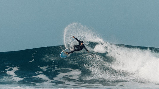 A surfer performing a maneuver while wearing the Manera Seafarer 5/4/3 hooded chest zip wetsuit.
